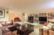 brown leather sofa in basedment with bookshelves tv and fireplace in the background