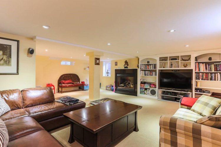 brown leather sofa in basedment with bookshelves tv and fireplace in the background